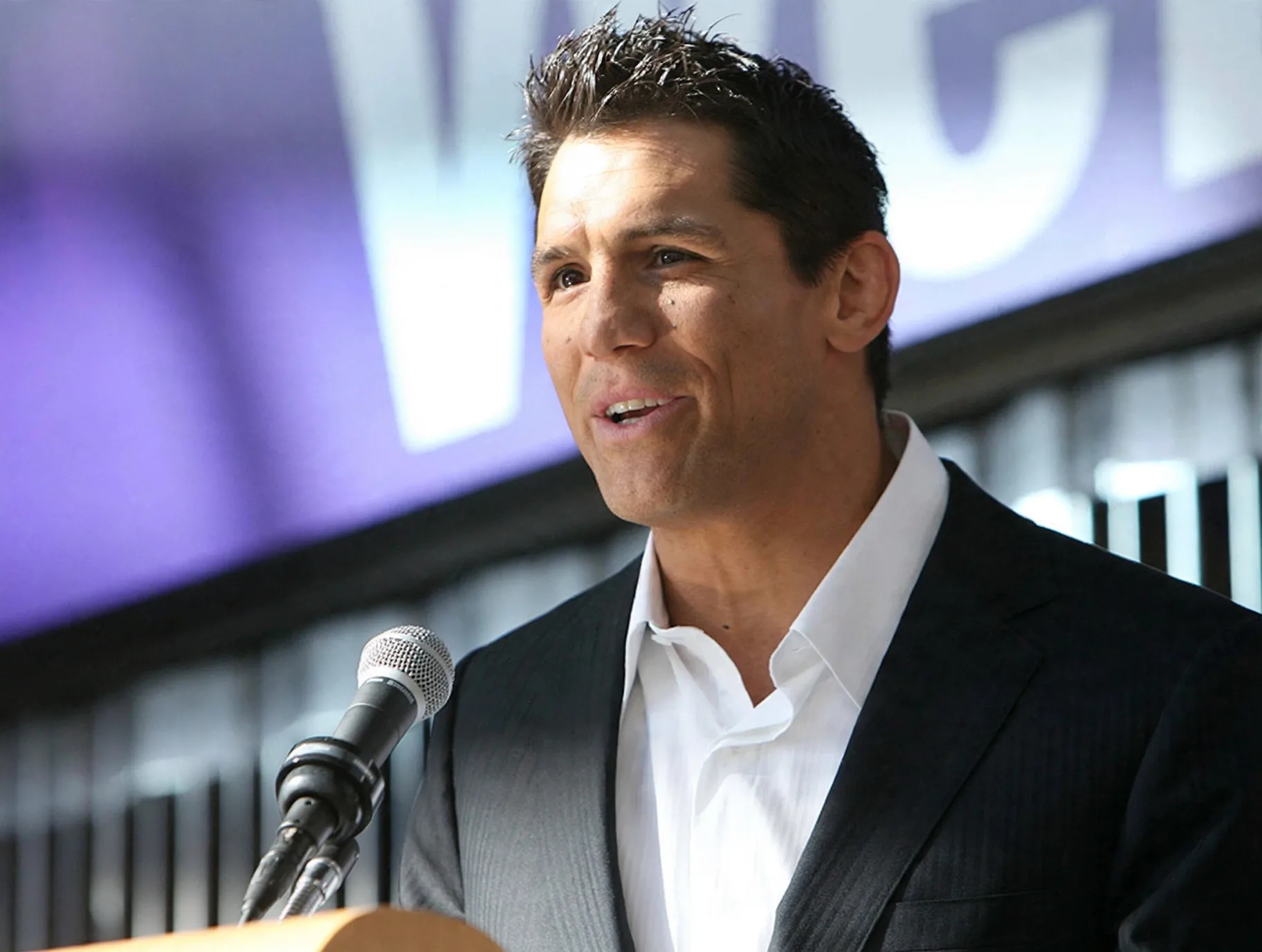 Frank Shamrock speaking at a podium in a dark suit and white shirt